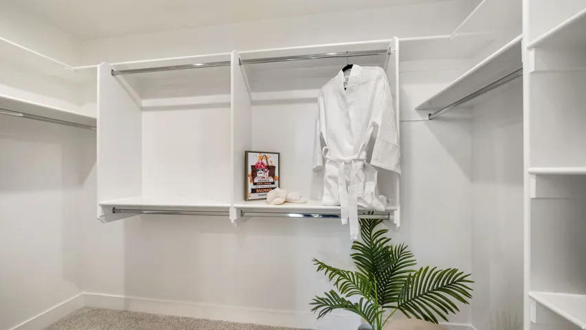 Spacious closet featuring white built-in shelving, chrome hanging rods, and light-toned carpeting