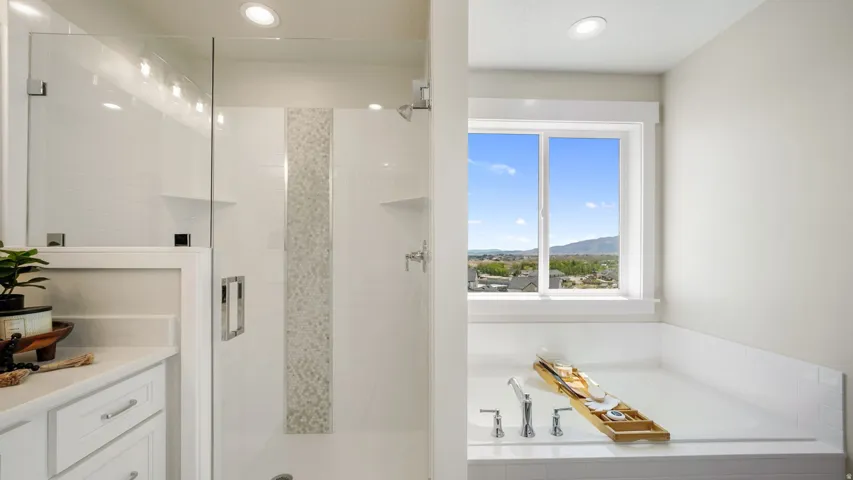 Spacious bathroom featuring a glass-enclosed shower with decorative tile accent, a built-in bathtub, and a window providing natural illumination