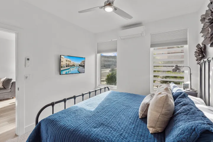 Bright bedroom featuring a ceiling fan with integrated lighting, wall-mounted display, and two windows with privacy blinds