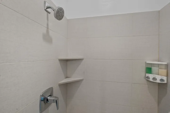 Shower enclosure featuring large format light-toned wall tiles, a chrome shower head, chrome single-handle valve, and built-in corner shelving