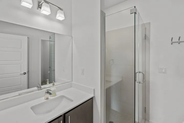 Bathroom featuring a glass-enclosed shower with a built-in bench, a vanity with an integrated sink, a large mirror, and wall-mounted lighting