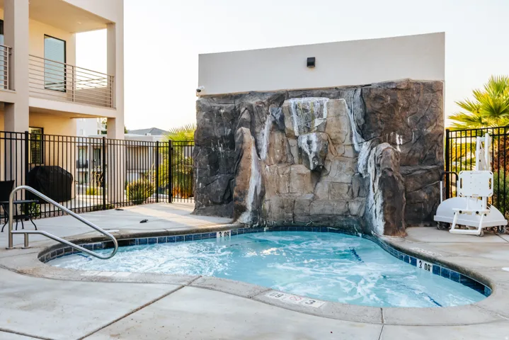 Bubbling spa featuring a rock waterfall, surrounding concrete patio, and dark tile border