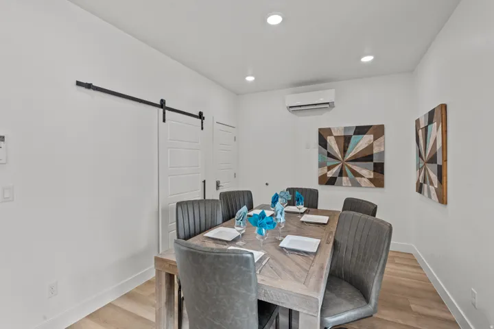 Dining area featuring light wood-finish flooring, recessed ceiling lighting, a barn door on a black rail, and a wall-mounted climate control unit