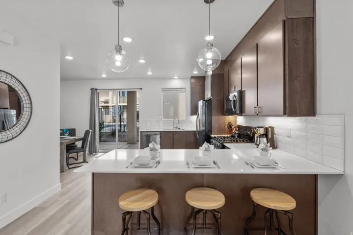 Modern kitchen featuring a breakfast bar with seating, white countertops, dark wood-finish cabinetry, and a subway tile backsplash