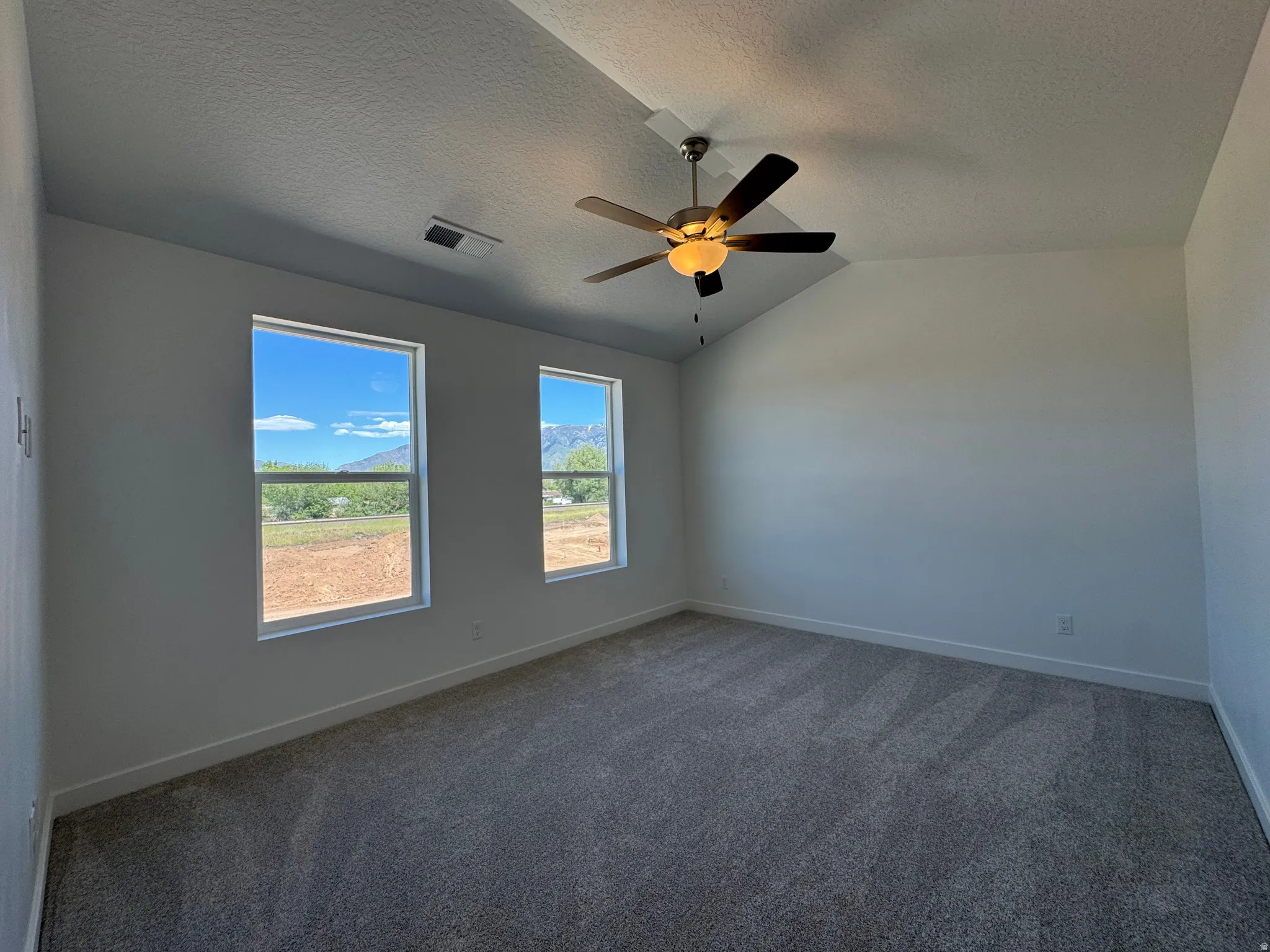 Spacious room featuring vaulted ceilings and a ceiling fan with integrated lighting