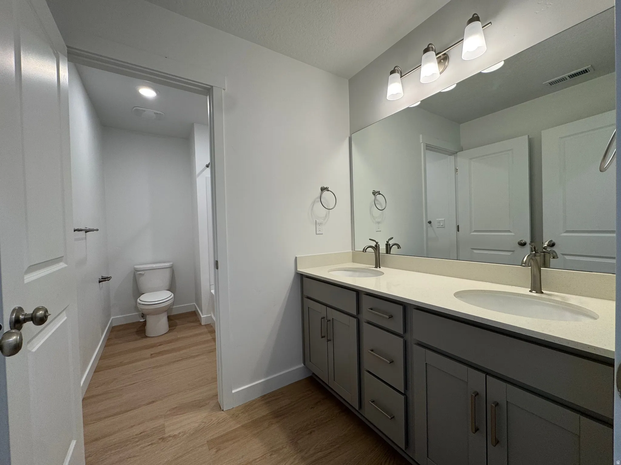 Dual vanity with gray cabinetry and light-toned countertops, featuring chrome fixtures and a wide mirror