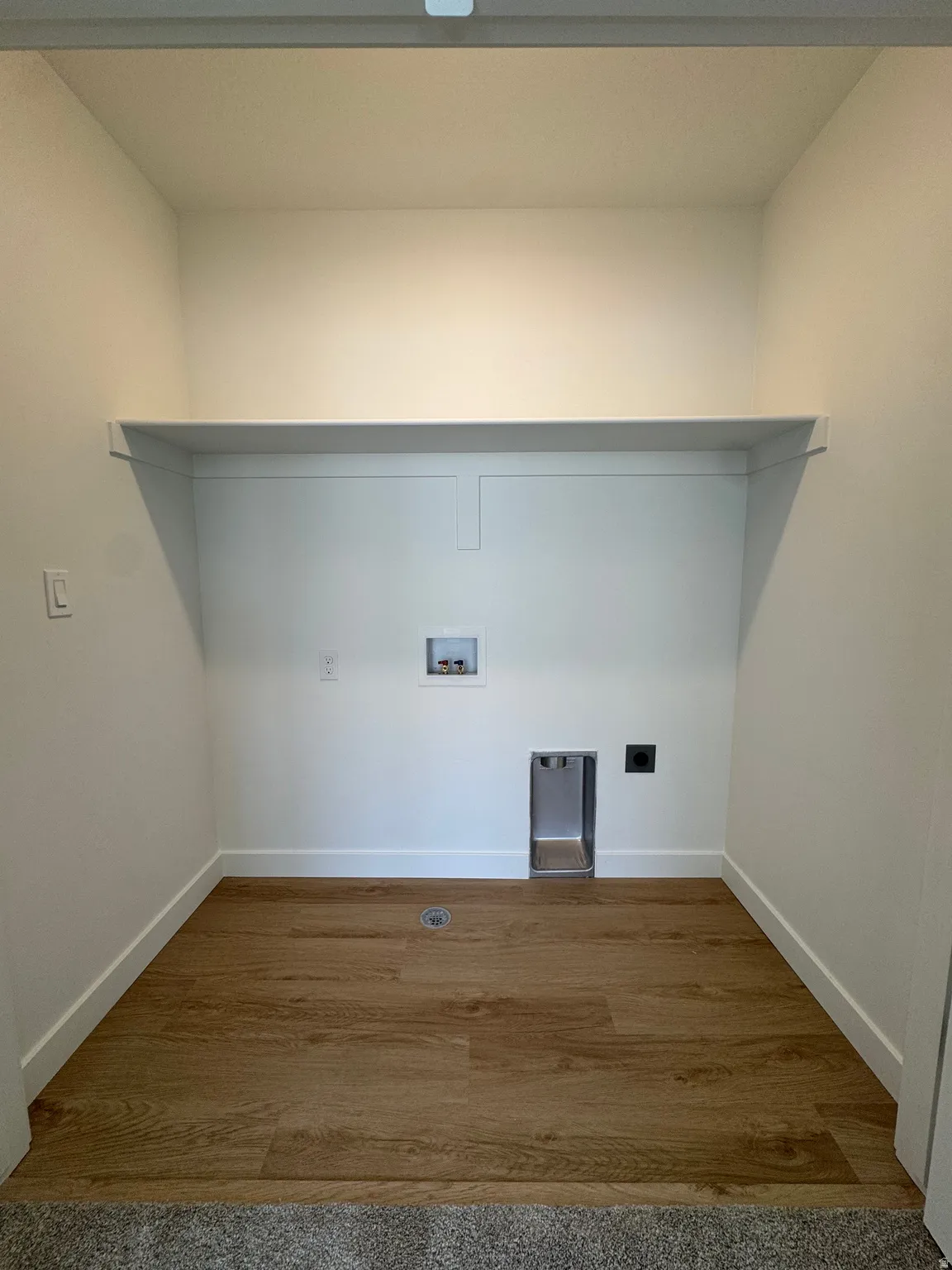 Dedicated laundry area featuring wood-finish flooring, a built-in shelf, and crisp white walls