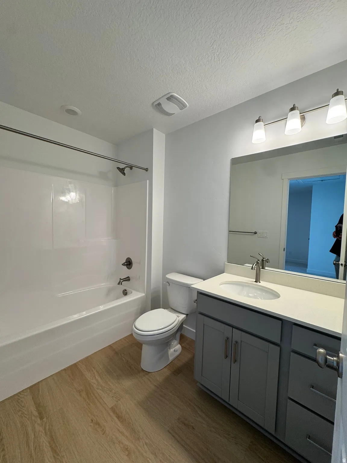Bathroom featuring a tub/shower combination with a shower rod, a toilet, a single vanity with a solid surface countertop, a rectangular mirror, and wood-finish flooring