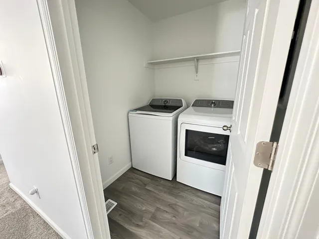 Dedicated laundry area featuring wood-finish flooring, white walls, and a built-in storage shelf
