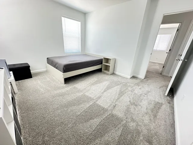Carpeted room with a single window featuring blinds, white walls, and a white baseboard trim