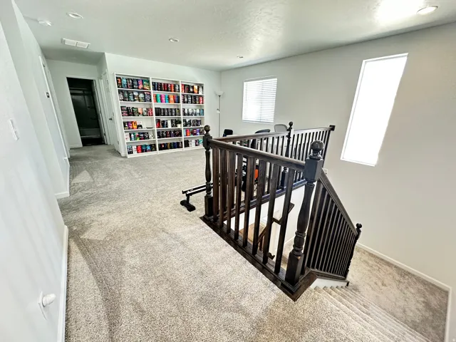 Versatile upstairs landing featuring dark wood balusters and railing, light gray carpet, recessed lighting, and multiple windows