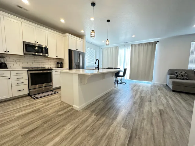 Open-concept living space featuring a kitchen island with seating, stainless steel appliances, white shaker cabinetry, subway tile backsplash, and light wood-finish flooring