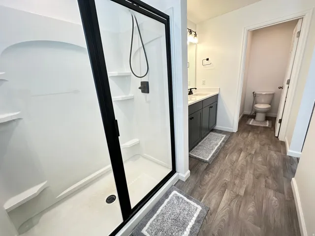 Bathroom featuring a black-framed glass shower enclosure, a dark gray vanity with a white countertop, and wood-finish flooring