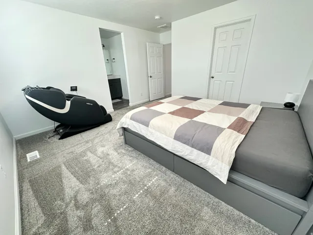Light gray carpeting throughout a bedroom featuring white walls and a white paneled door