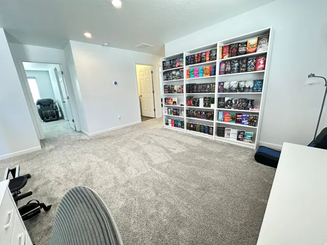Spacious room featuring light gray carpeting, recessed lighting, and a prominent built-in shelving unit