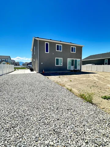 Two-story stucco exterior with white-framed windows, a sliding glass patio door, and a gravel surface alongside the structure
