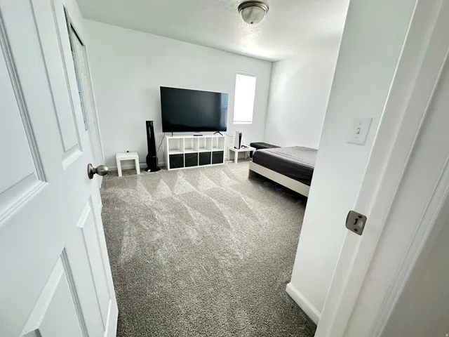 Carpeted room featuring a ceiling-mounted light fixture, white walls, and a window providing natural light