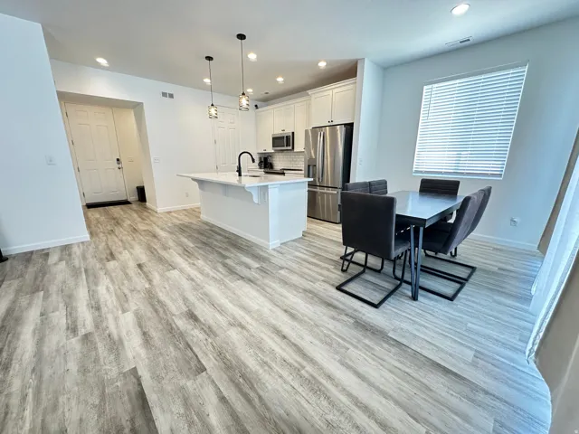 Contemporary kitchen featuring white cabinetry, a central island with a sink, stainless steel appliances, and pendant lighting