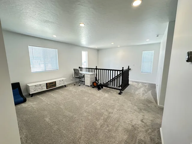 Spacious loft area featuring light-toned carpeting, recessed lighting, multiple windows with blinds, and a black spindle railing