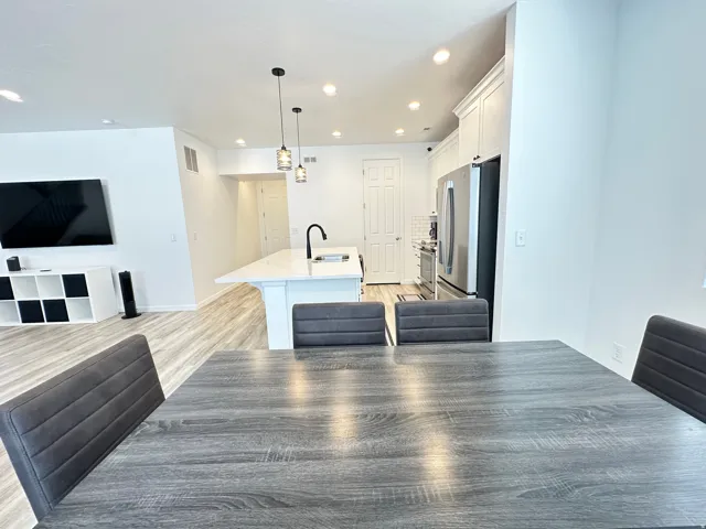 Modern kitchen featuring white cabinetry, stainless steel appliances, a center island with pendant lighting, and light wood-finish flooring