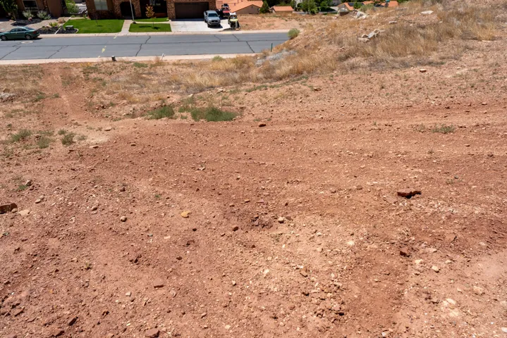 Terraced hillside lot featuring exposed red earth and scattered vegetation