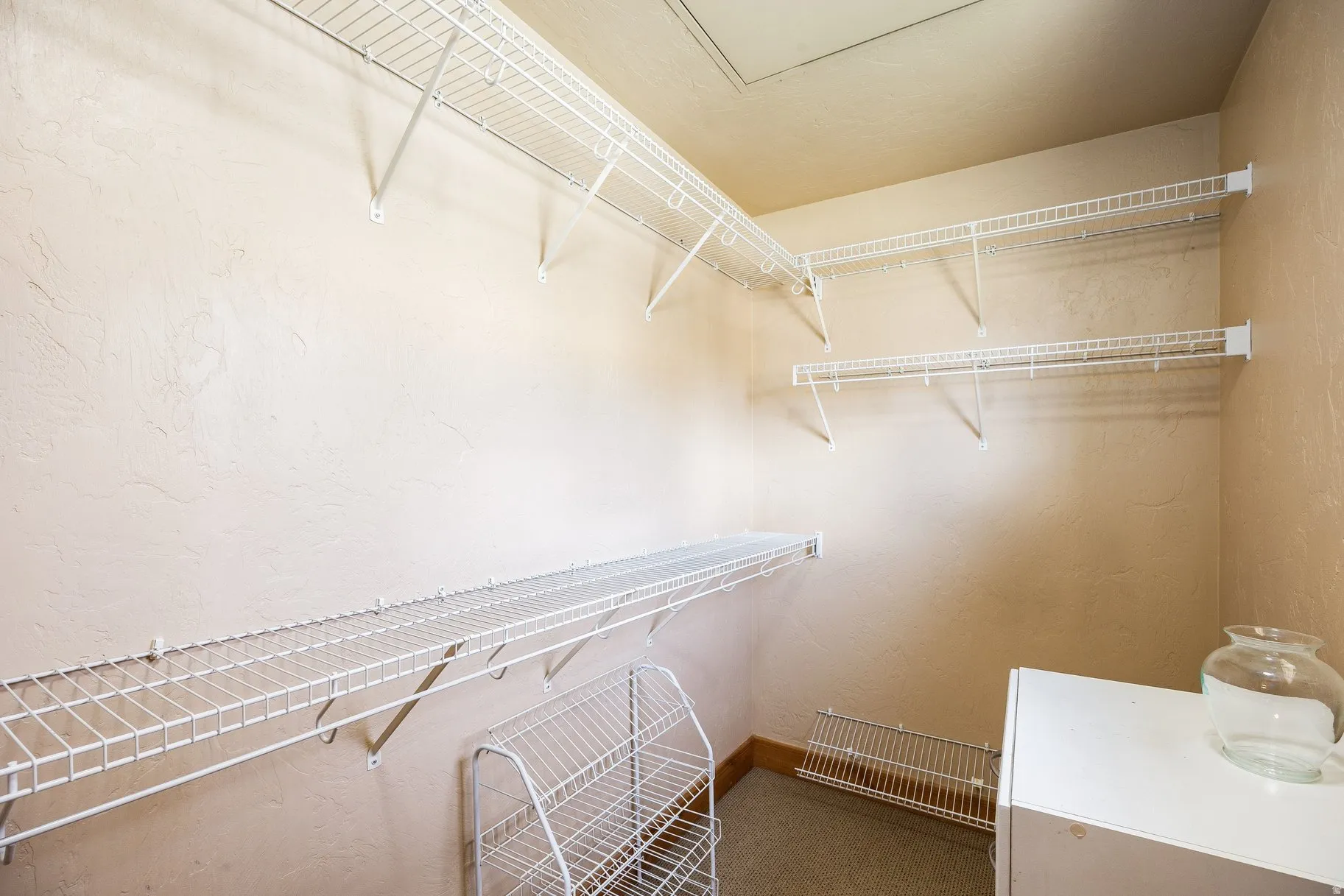 Interior closet space featuring multiple white wire shelving units and textured beige walls