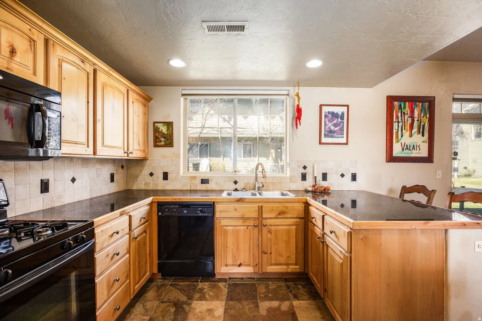 U-shaped kitchen featuring wood cabinetry, dark countertops, a tiled backsplash with diamond accents, and integrated black appliances including a gas range and dishwasher