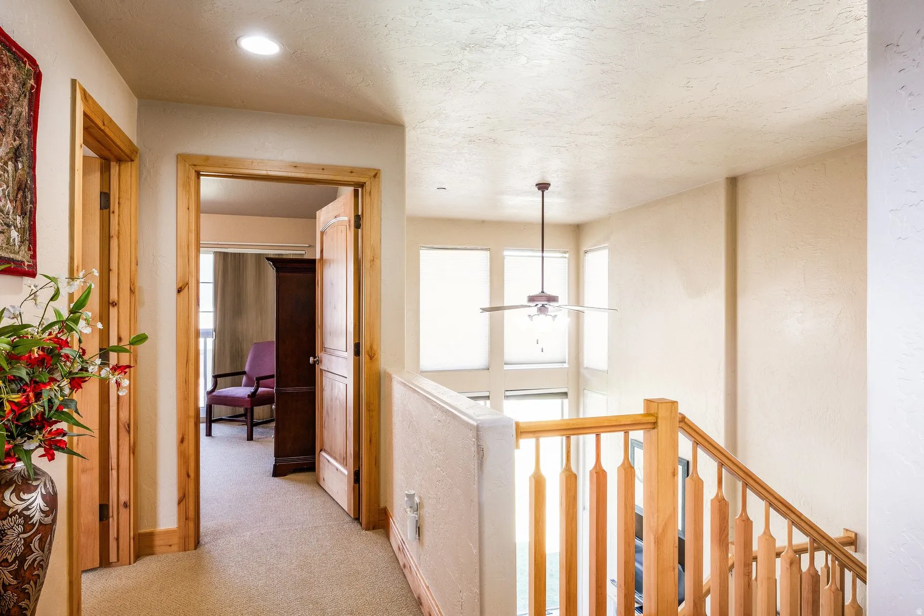 Upper-level hallway featuring a light wood staircase railing and banister, a recessed ceiling light, and a ceiling fan over the lower level