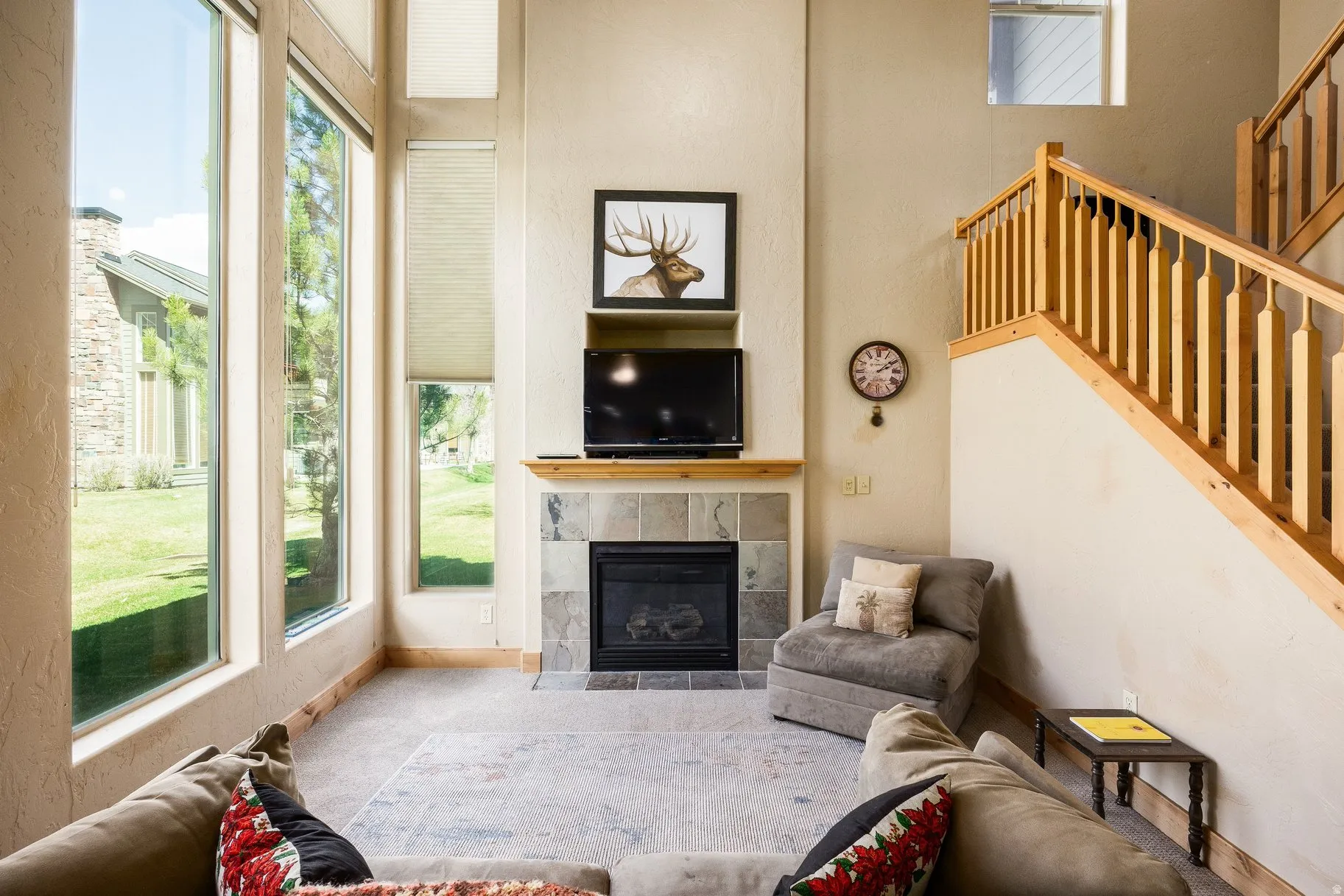 Two-story living area featuring a tile-surround fireplace with a wood mantle, an open staircase with a wood banister, and large vertical windows with blinds