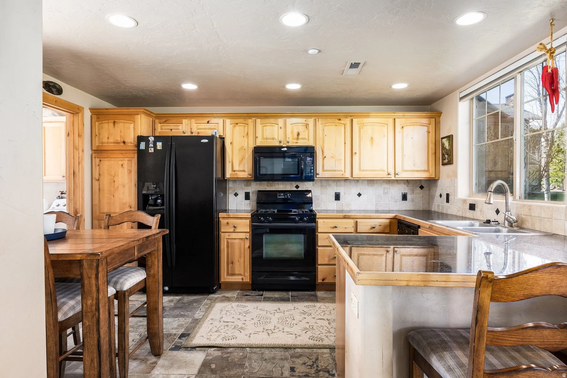 Kitchen featuring light wood cabinetry, dark-finish appliances, light-toned countertops, and mosaic tile backsplash