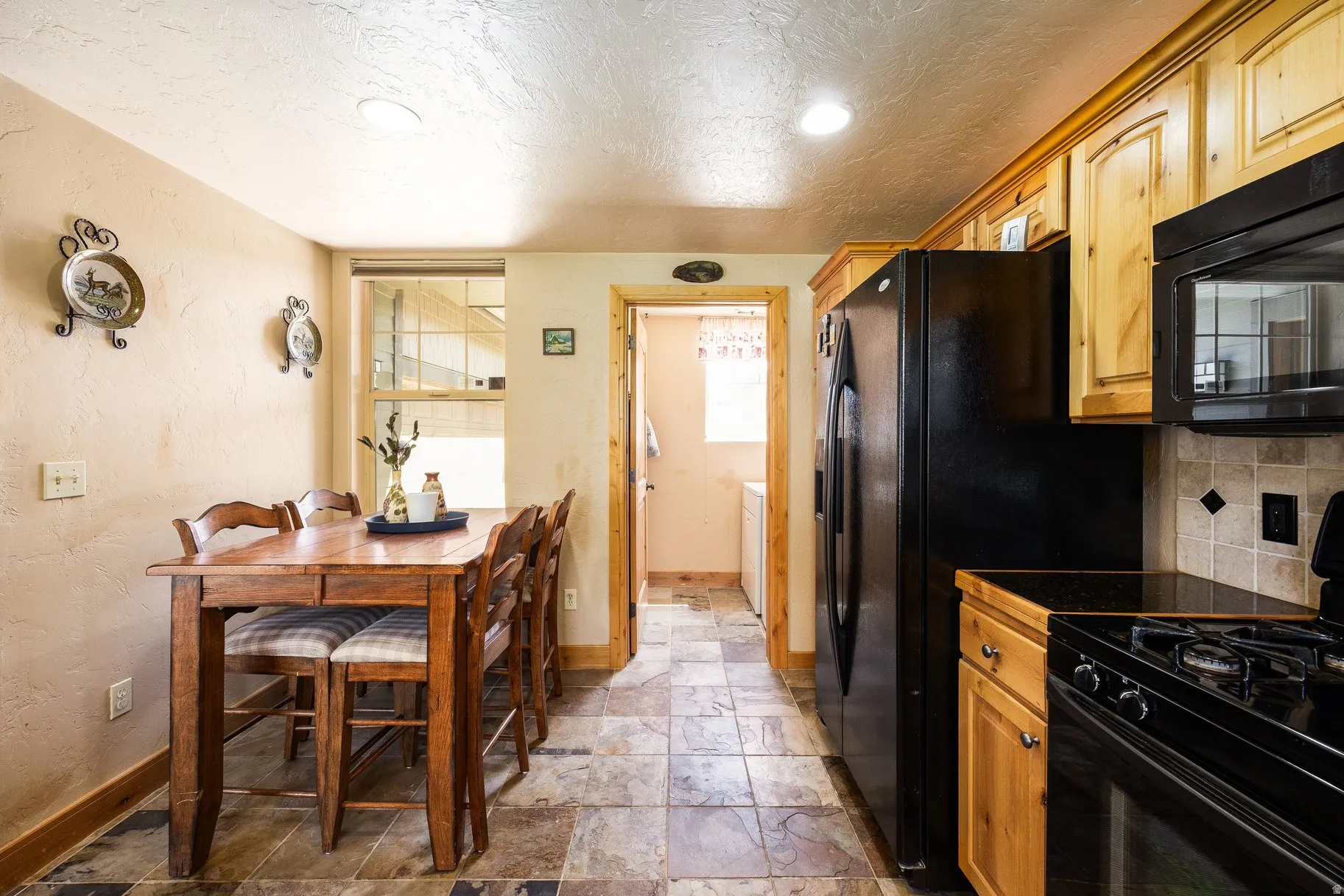 Kitchen featuring natural wood cabinetry, black appliances, stone tile flooring, and a coordinating stone tile backsplash