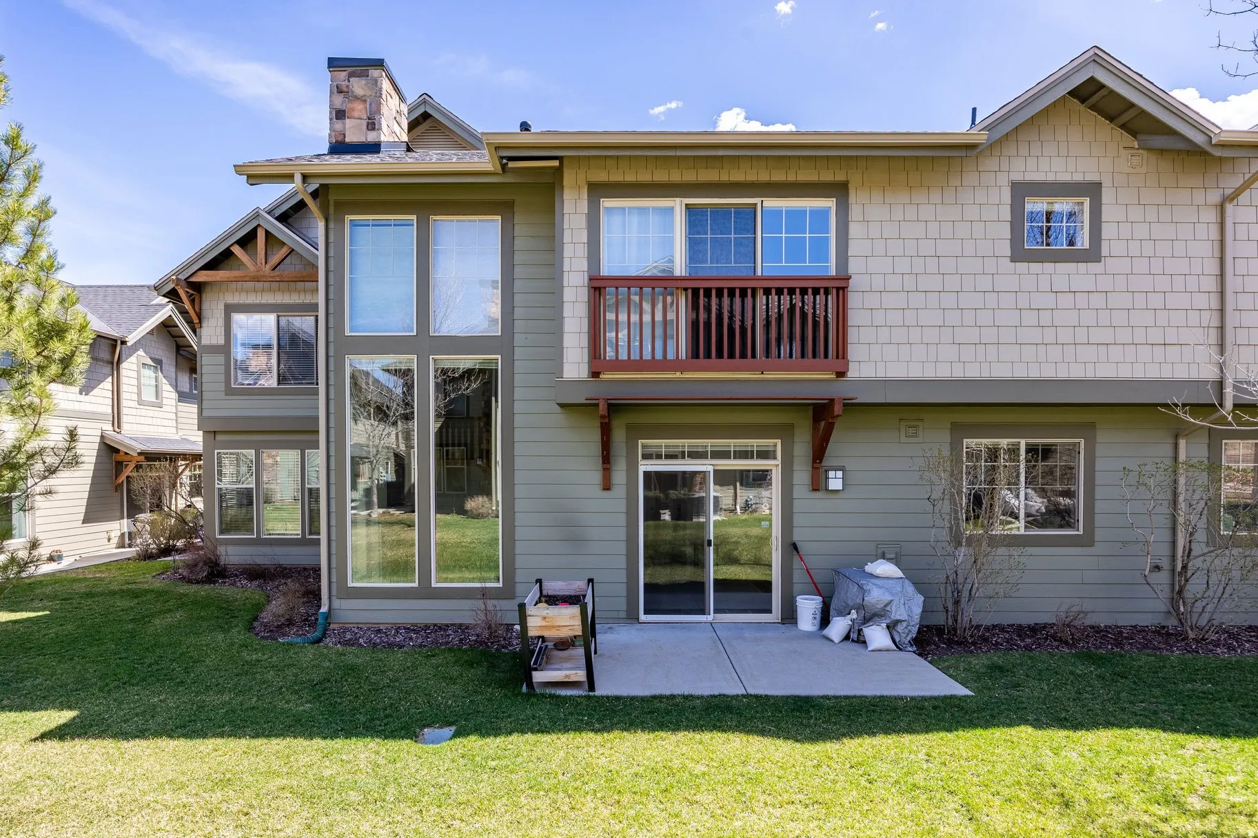 Rear exterior featuring a ground-level patio, upper-level balcony with wood railing, large vertical windows, and a stone chimney