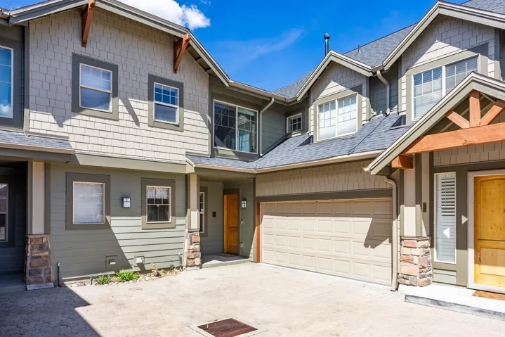 Modern townhome exterior featuring an attached garage, natural wood entry door, stone column accents, and shake siding details