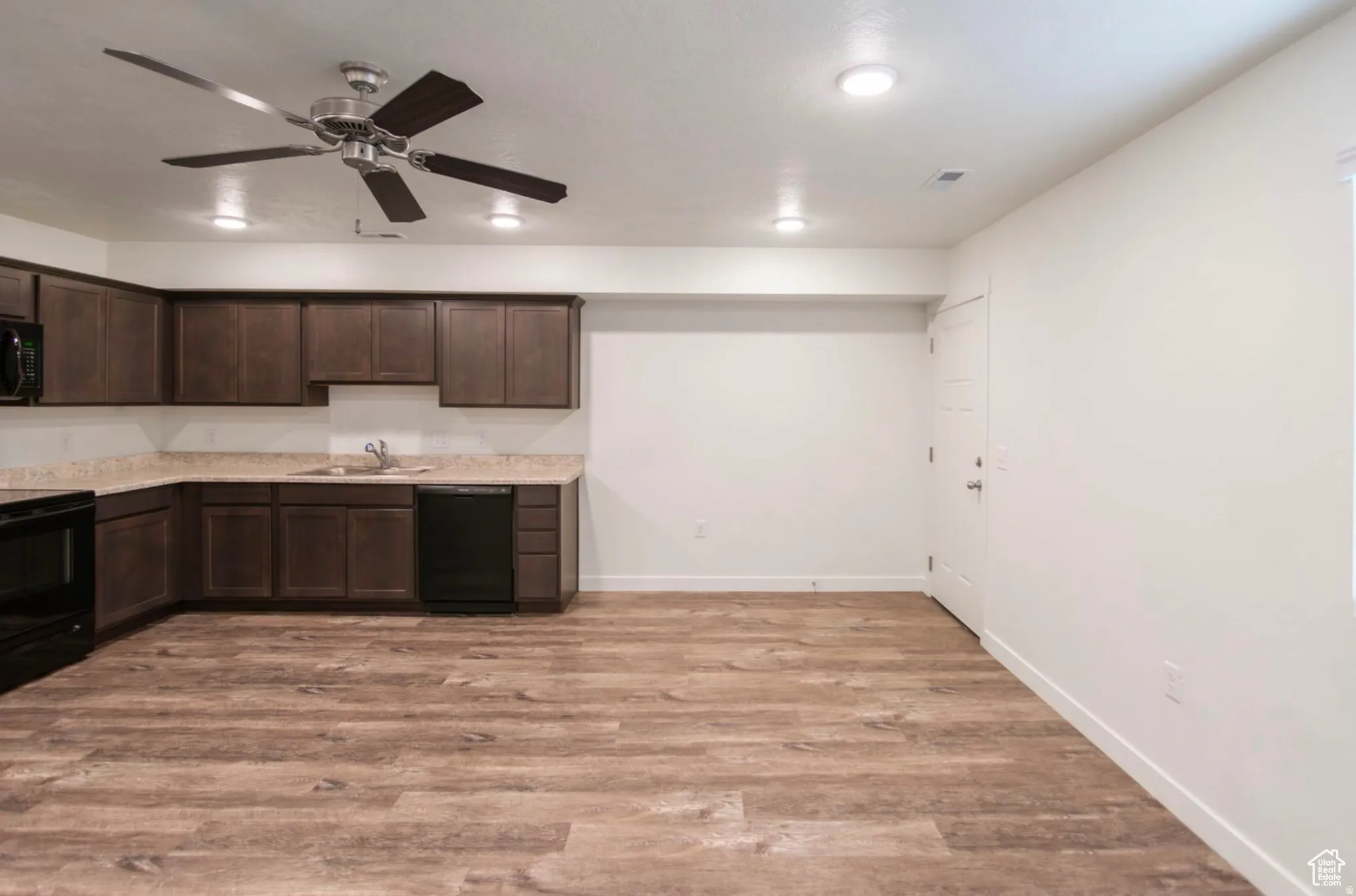 Kitchenette featuring dark wood cabinetry, light-toned countertops, and black appliances