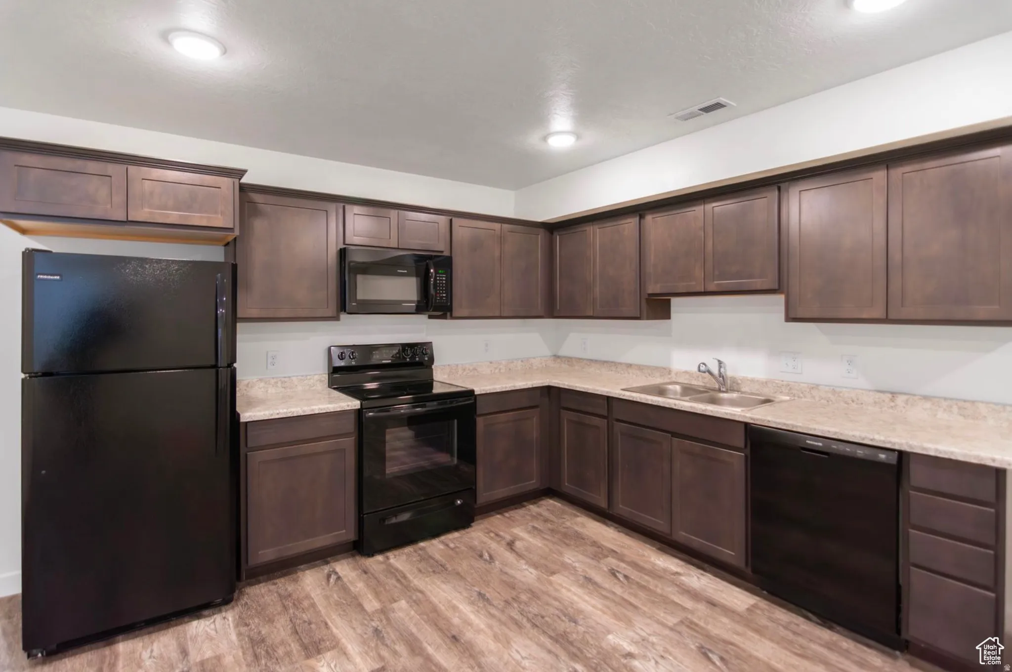 Kitchen featuring a full suite of black appliances, wood-finish flooring, dark wood cabinetry, and light-toned countertops