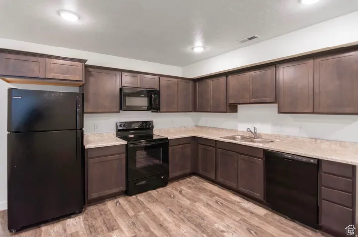 Kitchen featuring a full suite of black appliances, wood-finish flooring, dark wood cabinetry, and light-toned countertops