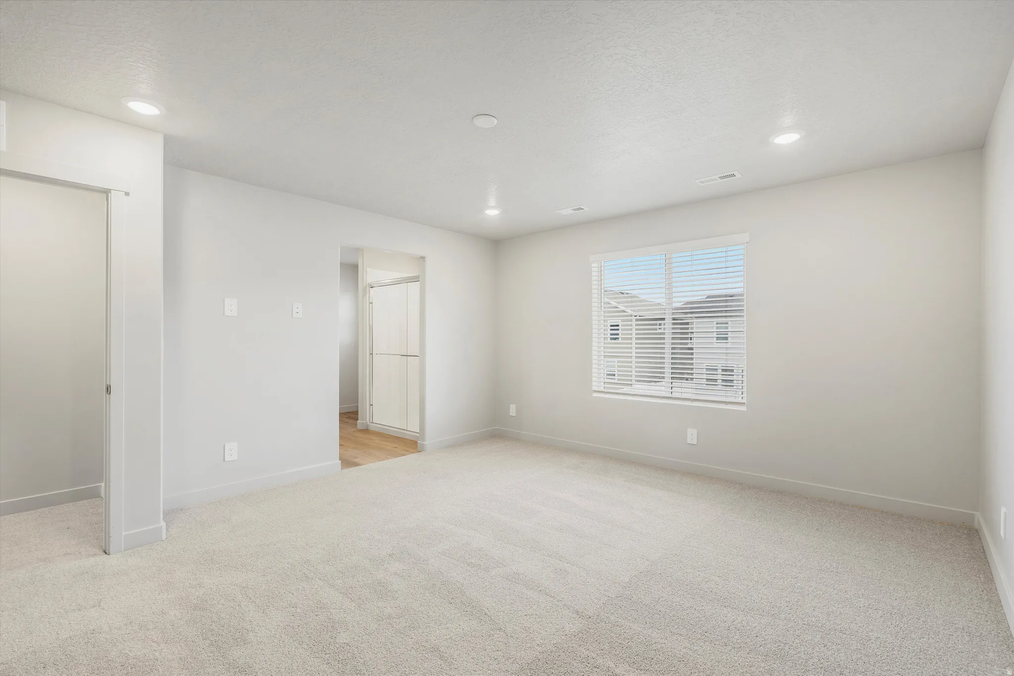 Spacious room featuring neutral carpeting, a large window with horizontal blinds, and recessed lighting