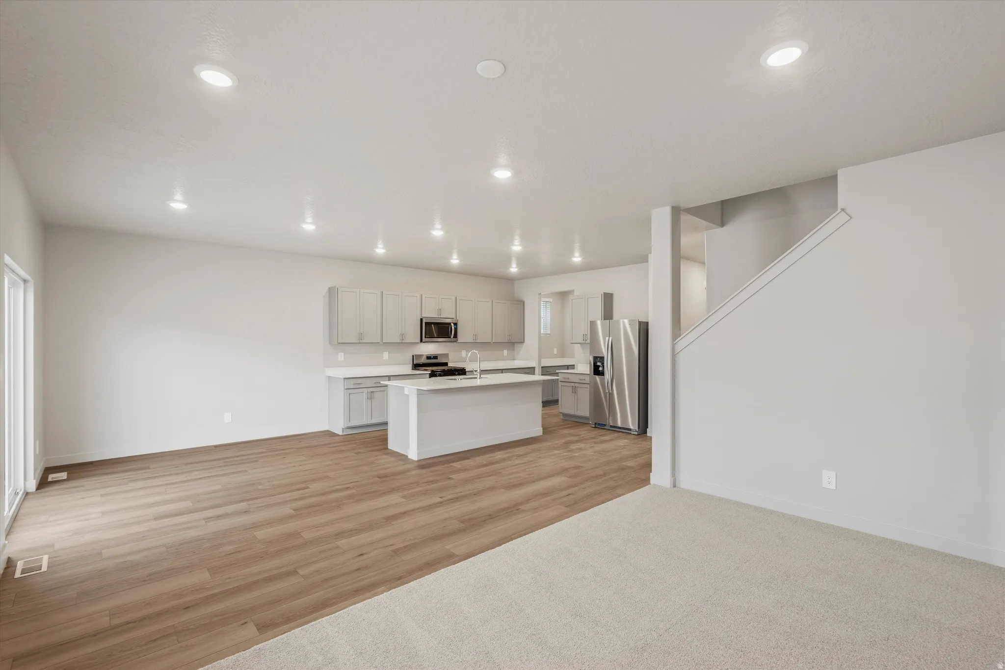 Open-concept living space featuring a modern kitchen with a central island, light cabinetry, and stainless steel appliances