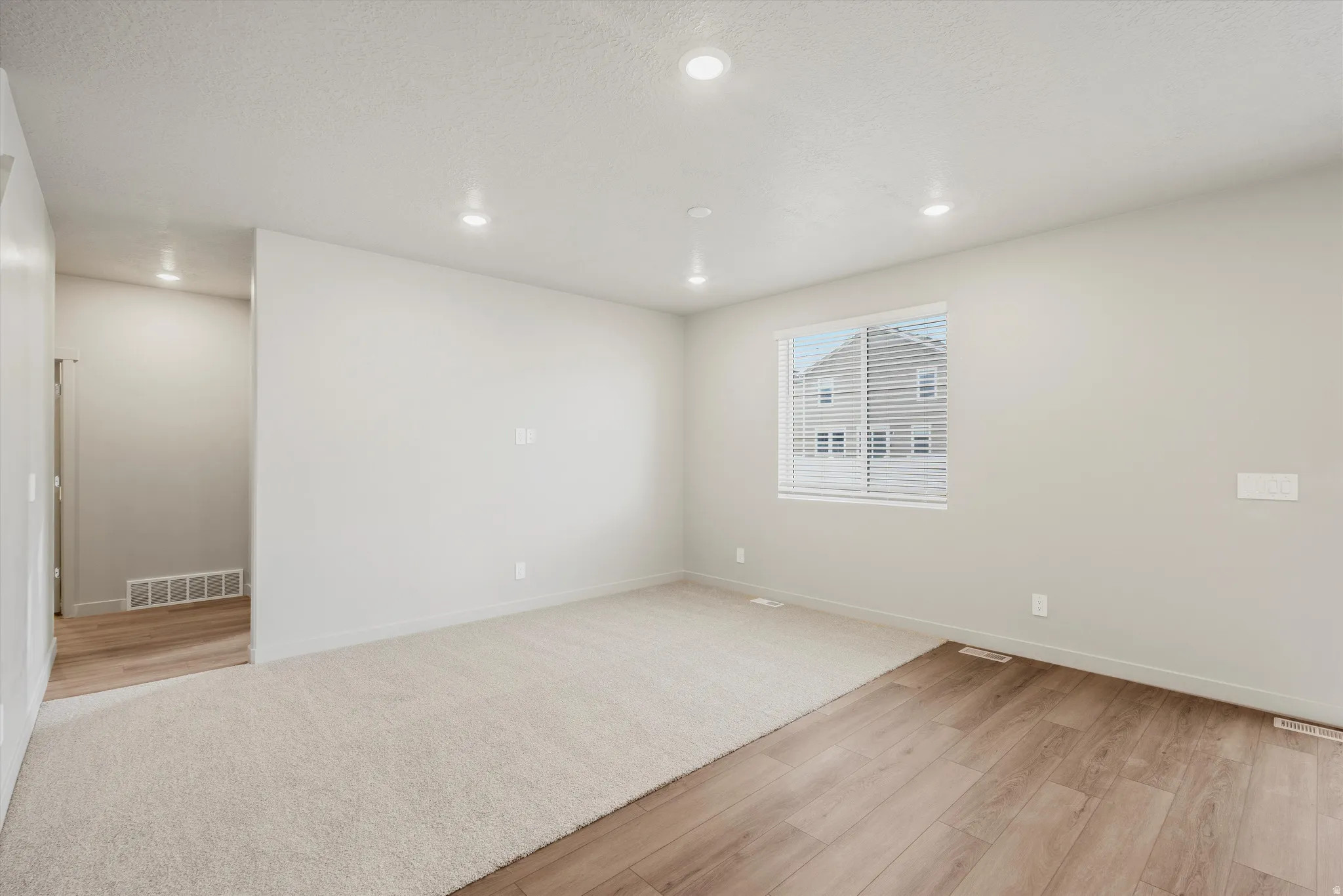 Spacious room featuring recessed lighting, a window with horizontal blinds, and a combination of light-toned carpeting and wood-finish flooring