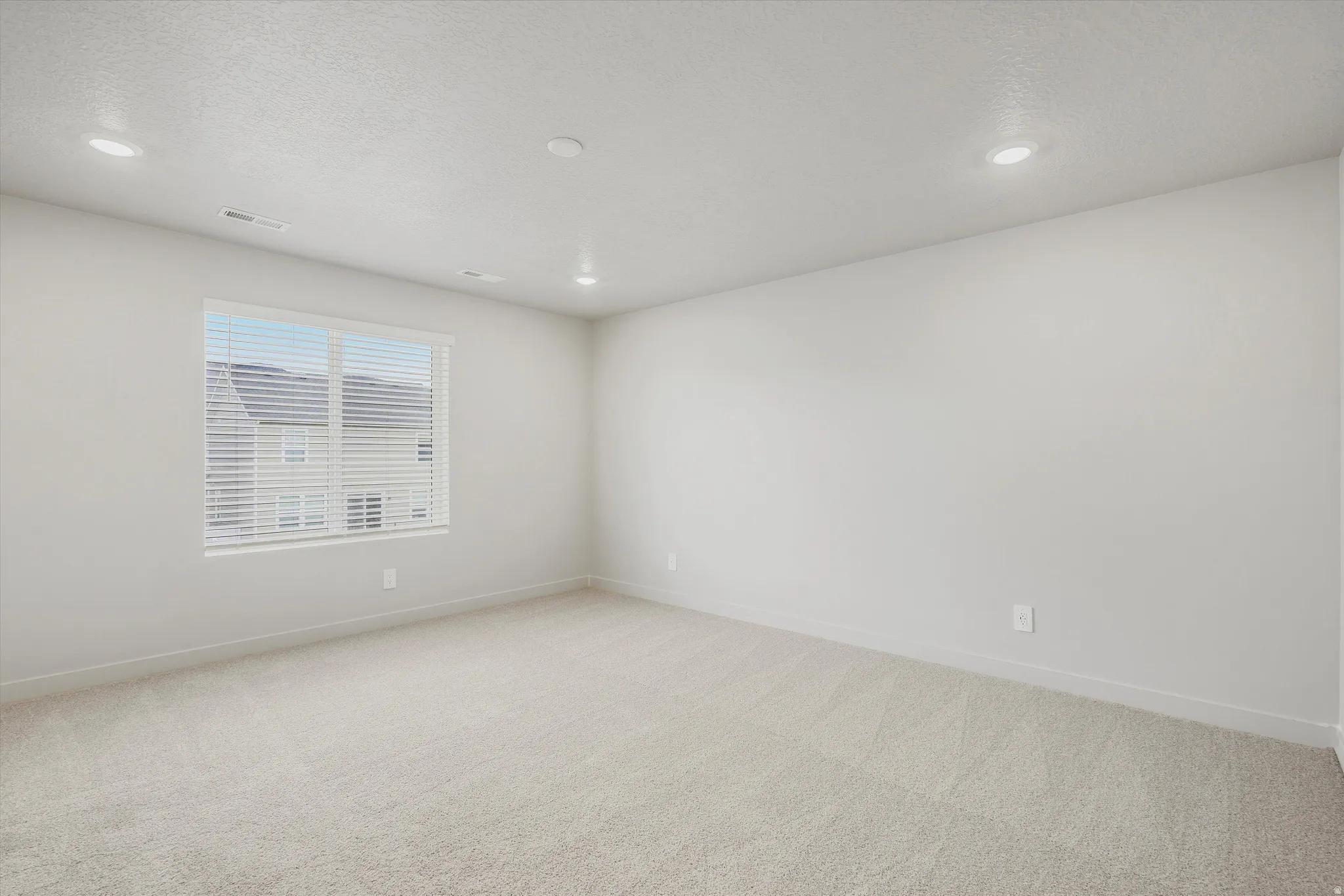Spacious room featuring neutral carpeting, light-colored walls, and a large window with blinds