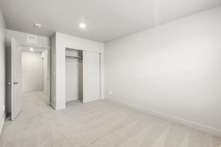 Spacious room featuring light-toned carpeting, white walls, recessed lighting, and a bi-fold closet with an integrated hanging rod