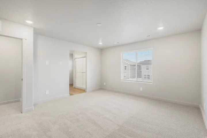 Spacious room featuring neutral carpeting, a large window with horizontal blinds, and recessed lighting