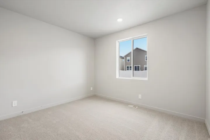 Neutral-toned interior room featuring light gray carpeting, matching baseboards, and a single window with white trim