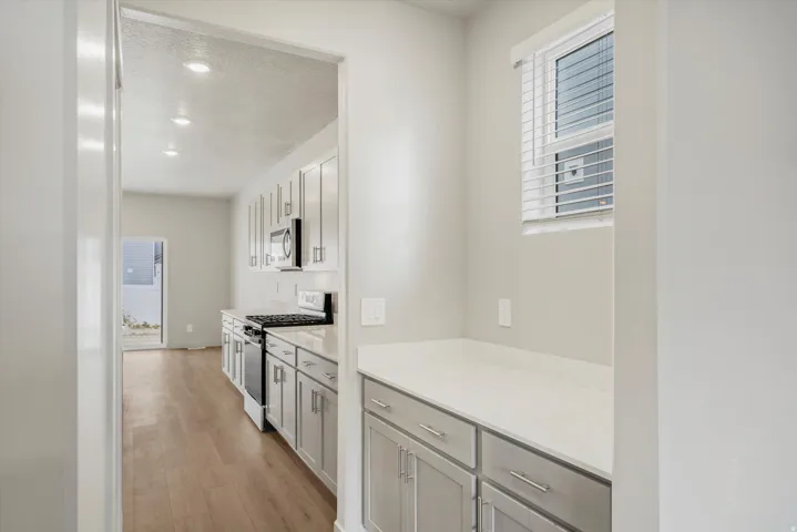Kitchen featuring white shaker cabinetry, stainless steel appliances, light-toned countertops, wood-finish flooring, and recessed lighting