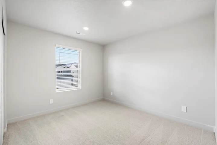 Carpeted interior space featuring a window with white blinds, recessed ceiling lighting, and light-toned wall paint