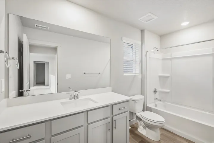 Bathroom featuring a white bathtub/shower combination, a single-sink vanity with light gray cabinetry, a white countertop, and wood-finish flooring