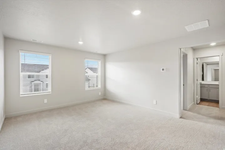 Spacious carpeted room featuring two windows with blinds, recessed lighting, and an entryway to a separate area with a vanity
