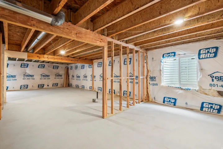 Unfinished basement space featuring exposed wood framing, concrete flooring, and an egress window