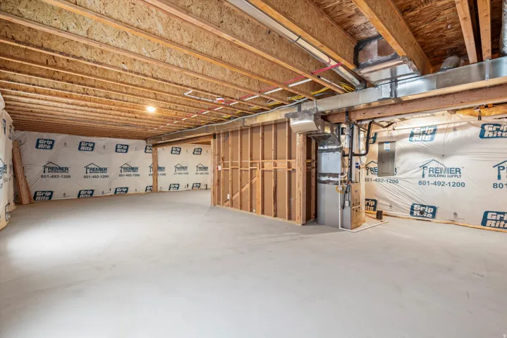 Unfinished basement featuring a spacious concrete floor, exposed wood ceiling joists, and framed walls