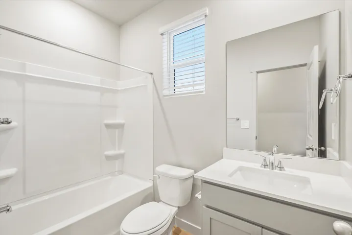 Bathroom featuring a white integrated tub and shower unit, a single vanity with a white countertop and undermount sink, a large wall-mounted mirror, and a window with blinds